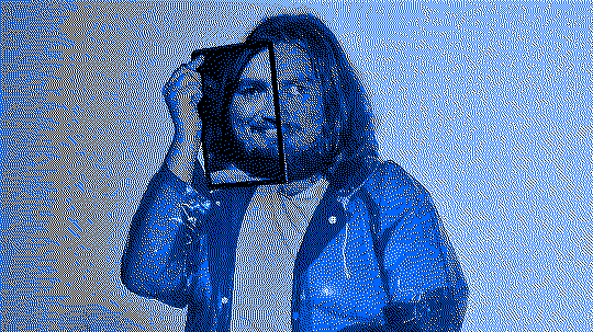 Chris in a blue transparent raincoat, holding a tablet with half of their face on it.